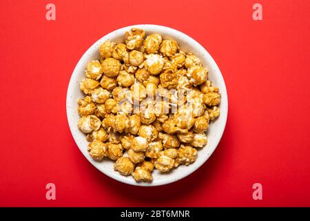 Plate with caramel popcorn on a red background Stock Photo