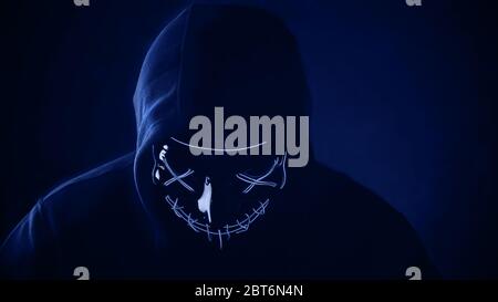 Man in scary lighting neon glow mask in hood in Phantom Blue color. Halloween and horror concept. Stock Photo