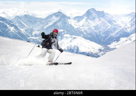 Female freerider skier rolls and rides on slope with powder snow spraying at beautiful alps mountain range. Winter season travel concept