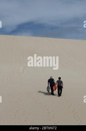 Kangaroo Island, Australia - March 9th, 2020: Two men climbing a sand dune for sand surfing. Stock Photo