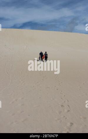 Kangaroo Island, Australia - March 9th, 2020: Two men climbing a sand dune for sand surfing. Stock Photo