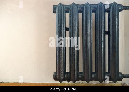 Old cast-iron radiator painted black against a white wall. Copy space. Stock Photo
