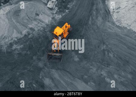 Yellow excavator or bulldozer in coal open cast mining quarry, aerial top view from drone. Stock Photo