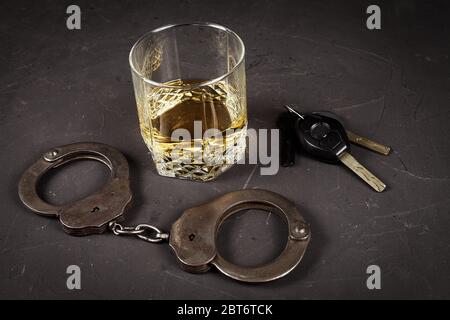 concept of criminal liability for driving while intoxicated. Bakal with cognac, handcuffs, car key on a dark background, vignetting Stock Photo
