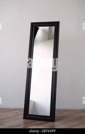 a rectangular mirror in a brown wooden frame stands indoors on a white background, Stock Photo