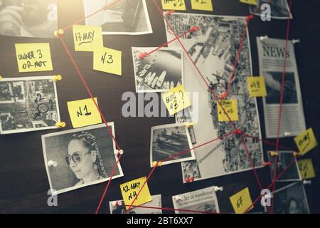 Detective board with crime scenes, photos of suspects and victims, evidence with red threads, vintage toned Stock Photo