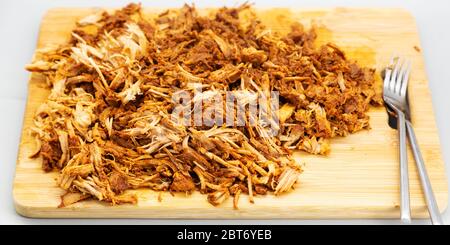 Homecooked pulled pork served shredded on a wooden board. The dish has been prepared in a slow cooker and cooked for nine hours. Stock Photo