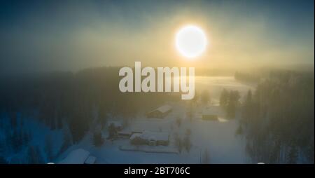 Majestic view of winter sunset with very large sun spot in frozen foggy air, winter pine tree forest, aerial, Grano village, around Umea city, Norther