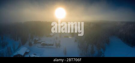 Majestic view of winter sunset with very large Sun spot in frozen foggy air, winter pine tree forest, aerial, Grano village, around Umea city, Sweden