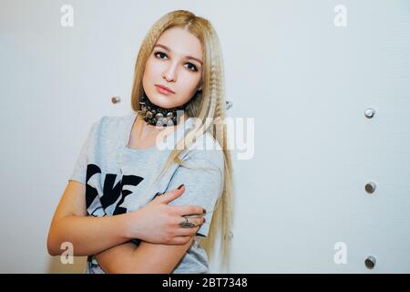 Portrait of a pretty blonde teenage girl. She has long waffled blonde hair and is wearing a t-shirt and a choker with metal pieces around her neck