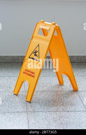 Caution wet floor or cleaning in progress. A yellow sign warns of danger. Stock Photo