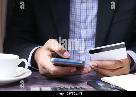 Man in suit holding credit card and using smart phone, online shopping concept Stock Photo