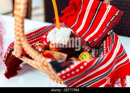 Kulich Russian Orthodox Easter blessing wicker straw basket on table with traditional red embroidered towel in church and dessert cake candle and eggs Stock Photo