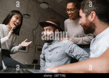 Image of multiethnic young female and male colleagues discussing business ideas at table while working in office Stock Photo