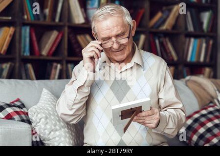 Senior man alone sitting at library looking at family picture smiling happy Stock Photo