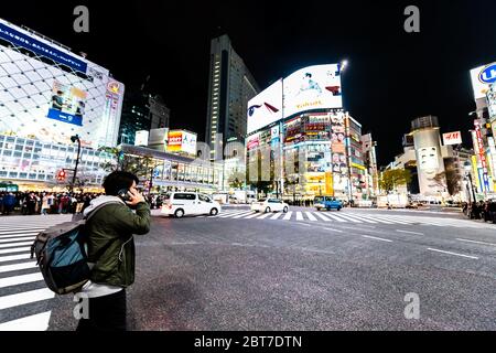 Shibuya, Japan - April 1, 2019: Famous crossing in downtown city with billboard advertisement lights and people waiting to cross at evening night in T Stock Photo