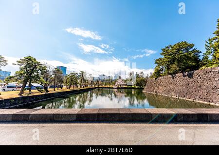 Tokyo, Japan - April 1, 2019: Reflection in moat lake by Imperial palace during spring day with cityscape skyscrapers in downtown park wide angle view Stock Photo