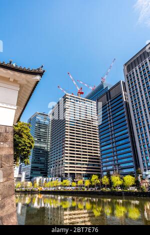 Tokyo, Japan - April 1, 2019: Moat water and surrounding wall by Imperial palace during spring day with cityscape skyscrapers in downtown park vertica Stock Photo