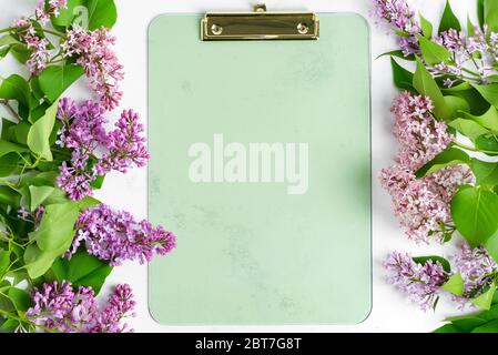 Congratulation postcard with frame from fresh branches of lilac flowers and mock up clipboard for message on a light grey marble background, copy spac Stock Photo