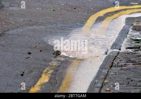 Rainwater pouring over blocked surface water road drain, UK Stock Photo