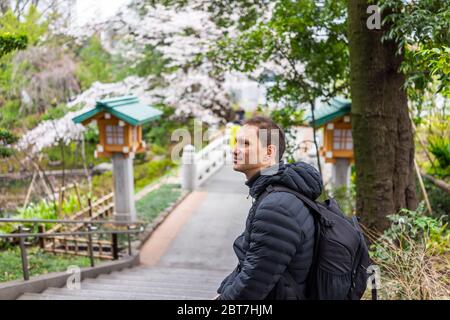 Tokyo, Japan Togo shrine temple garden with one foreigner tourist man sitting on railing of steps on street in Shibuya Harajuku with cherry blossom in Stock Photo