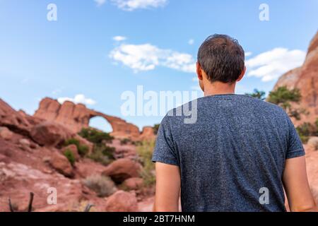 Arches National Park with Skyline Arch canyon in background and back of young man standing looking at view on trail hike in Utah Stock Photo