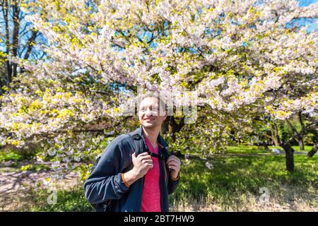 Tokyo, Japan spring springtime at Imperial Palace garden park with young happy tourist man smiling by sakura flowers cherry blossom tree wide angle vi Stock Photo