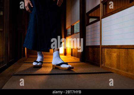 Japanese ryokan traditional house room low angle view with man in kimono closeup of legs feet with tabi white socks and geta shoes walking by shoji sl Stock Photo