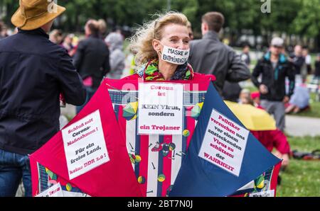 Munich, Bavaria, Germany. 23rd May, 2020. A woman holds an umbrella with many of the talking points of those against the Coronavirus measures and ''Mask of Prohibition (of speech) on her mouth. After days of back and forth wrangling with the Munich Kreisverwaltungsreferat, the organizers of the so-called 'Hygiene Demo'' in Munich were again granted permission for 1,000 distanced participants inside the demo area only to have torrential downpours and dangerous winds cause a cancellation for the 500 that arrived.Further being criticized by politicians, civic groups and healthcare workers are Stock Photo