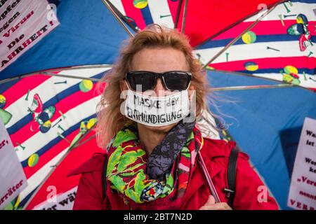 Munich, Bavaria, Germany. 23rd May, 2020. A woman holds an umbrella with many of the talking points of those against the Coronavirus measures and ''Mask of Prohibition (of speech) on her mouth. After days of back and forth wrangling with the Munich Kreisverwaltungsreferat, the organizers of the so-called 'Hygiene Demo'' in Munich were again granted permission for 1,000 distanced participants inside the demo area only to have torrential downpours and dangerous winds cause a cancellation for the 500 that arrived.Further being criticized by politicians, civic groups and healthcare workers are Stock Photo