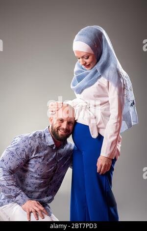 Happy couple expecting baby on the gray background. Father listening. Stock Photo