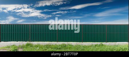 Green metal fence. Blue sky with clouds. Front view. Stock Photo