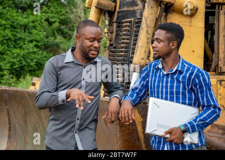 two young african business men, discussing while standing next to a tractor Stock Photo