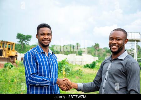 two african business men shake hands, smiling as they are satisfied with a deal Stock Photo