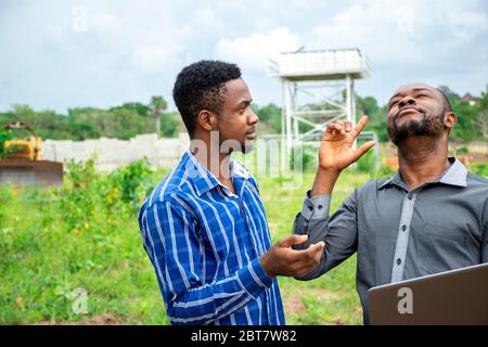 two african business men, discussing using a laptop on a piece of land Stock Photo