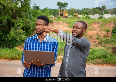 two young african business men, discussing and surveying a piece of land, using a laptop Stock Photo