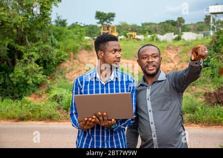 two young african business men, discussing and surveying a piece of land, also using a laptop Stock Photo