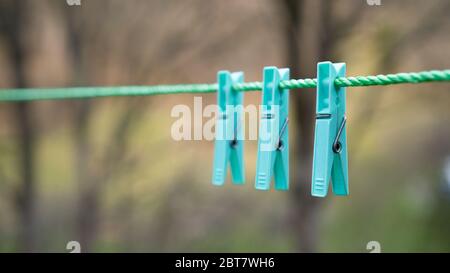 Group of one color clothespins hanging on a rope. Clothespins on Clothes line on green blurred background. Pegs Stock Photo