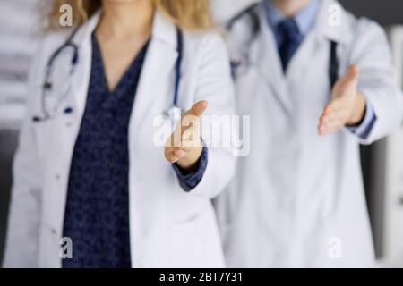 Two doctors standing and offering helping hand for shaking hand or saving life. Medical help, countering viral infection and medicine concept Stock Photo
