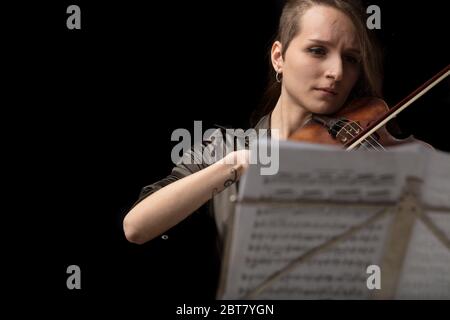 Woman violinist playing in a classical recital on a baroque violin viewed over the top of a music score on a brass stand during the live performance Stock Photo