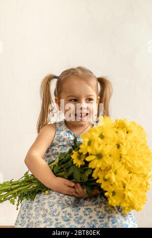 childhood, holidays, flowers, gifts concept - little cute three year old girl with two ponytails on her head in blue colorful dress holds large Stock Photo