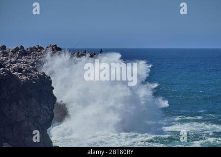 Waves clashing at the cliffs of Carrapateira Beach, with people on the cliffs Stock Photo