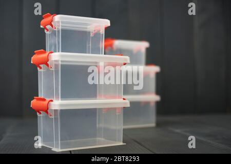 Clear plastic object storage boxes with orange accents stacked on floor and gray wooden background Stock Photo