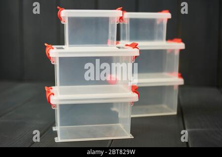 Clear plastic object storage boxes with orange accents stacked on floor and gray wooden background Stock Photo