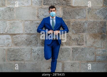 Young and stylish business man with face mask stands on old stone wall Stock Photo