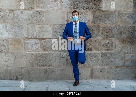 Young and stylish business man with face mask stands on old stone wall Stock Photo
