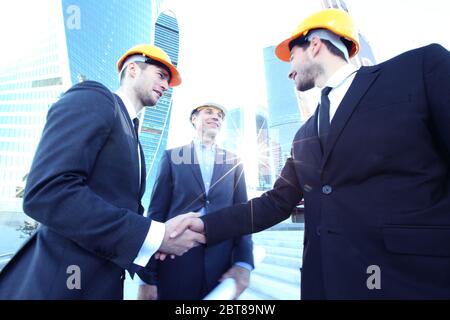 Architect and engineers shaking hands at construction site, skyscrapers on background Stock Photo