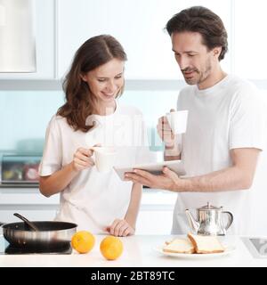 Couple cooking breakfast together in kitchen using tablet pc Stock Photo