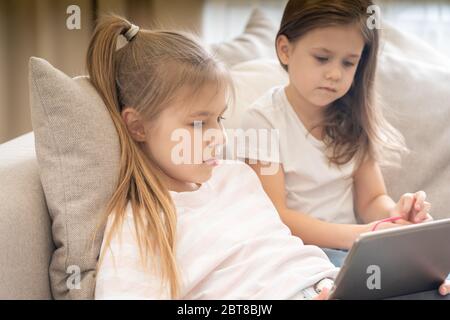 Two sisters Lying On Couch And Using Tablet Stock Photo