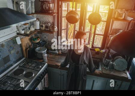 Portrait of mature woman in an old narrow cluttered kitchen at sunset Stock Photo